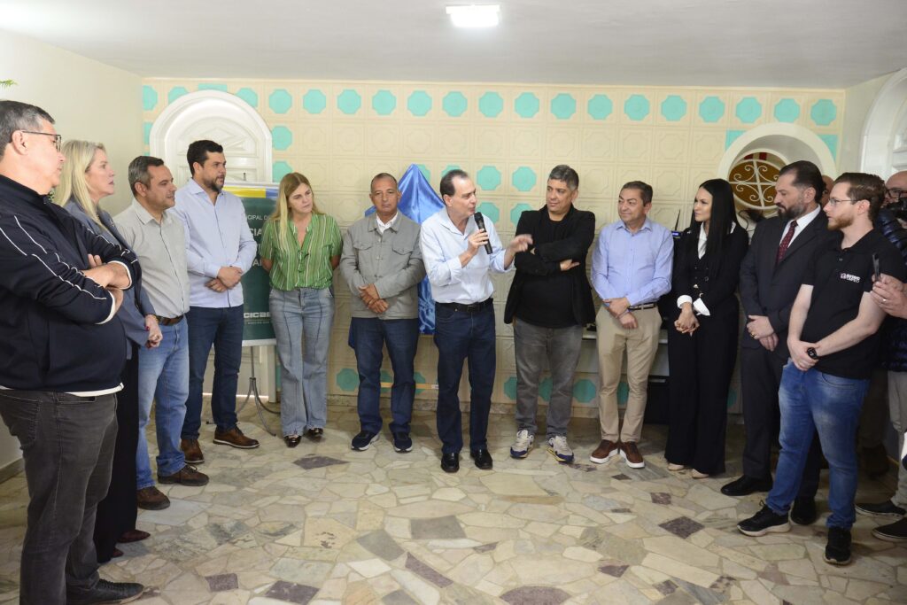 A imagem mostra um grupo de pessoas reunidas em um ambiente interno para uma inauguração oficial. No centro, há uma placa metálica sobre um cavalete de madeira com o título “Inauguração Residência Inclusiva”, indicando que o evento celebra a abertura de uma instituição voltada à inclusão social.