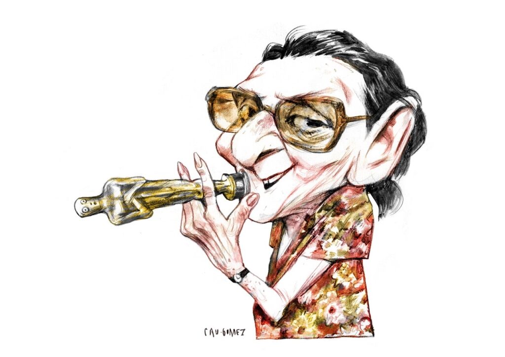 A imagem mostra uma caricatura desenhada à mão de um homem tocando um instrumento de sopro dourado, parecido com um trompete ou uma corneta. Ele usa óculos grandes de armação marrom, tem cabelos escuros penteados para trás, nariz e orelhas exagerados e uma expressão sorridente. O homem veste uma camisa florida em tons de vermelho, amarelo e verde, além de um relógio no pulso. O fundo é branco, e a assinatura “CAV-GOMEZ” aparece na parte inferior da ilustração.