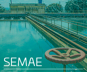 A imagem mostra uma estação de tratamento de água, com um grande tanque de água e diversas estruturas metálicas, incluindo corrimãos e tubulações. No primeiro plano, há uma grande válvula vermelha. Ao fundo, é possível ver um edifício e algumas árvores. O texto "SEMAE" está destacado no canto inferior esquerdo da imagem.