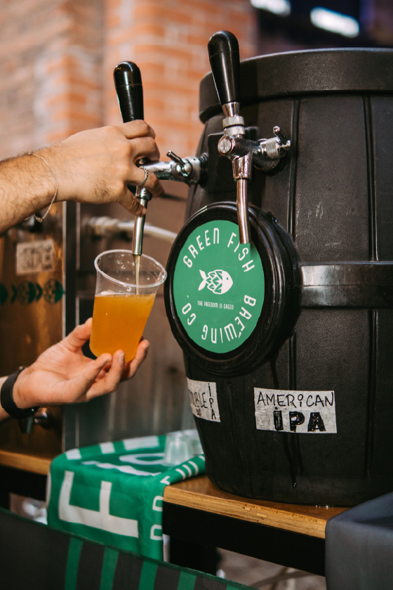 Um barril de cerveja artesanal preto com a marca verde da "Green Fish Brewing Co." sobressai num balcão, no âmbito da divulgação para a 3ª Oktoberfest de Piracicaba