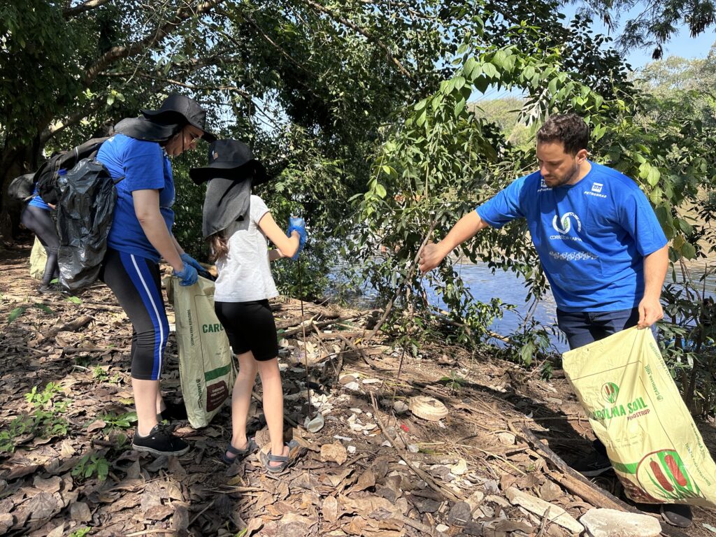 voluntários recolhem lixo e materiais descartados nas margens do rio, utilizando sacos e equipamentos de proteção.