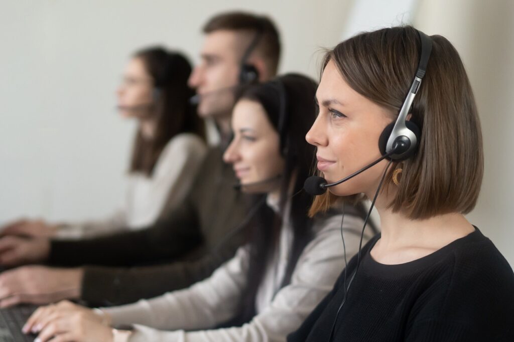 Equipe de atendimento ao cliente trabalha em central de suporte com uso de headsets e computadores.