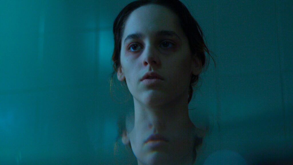 close de uma jovem em ambiente com iluminação azulada e reflexos desfocados, criando uma atmosfera introspectiva e cinematográfica.