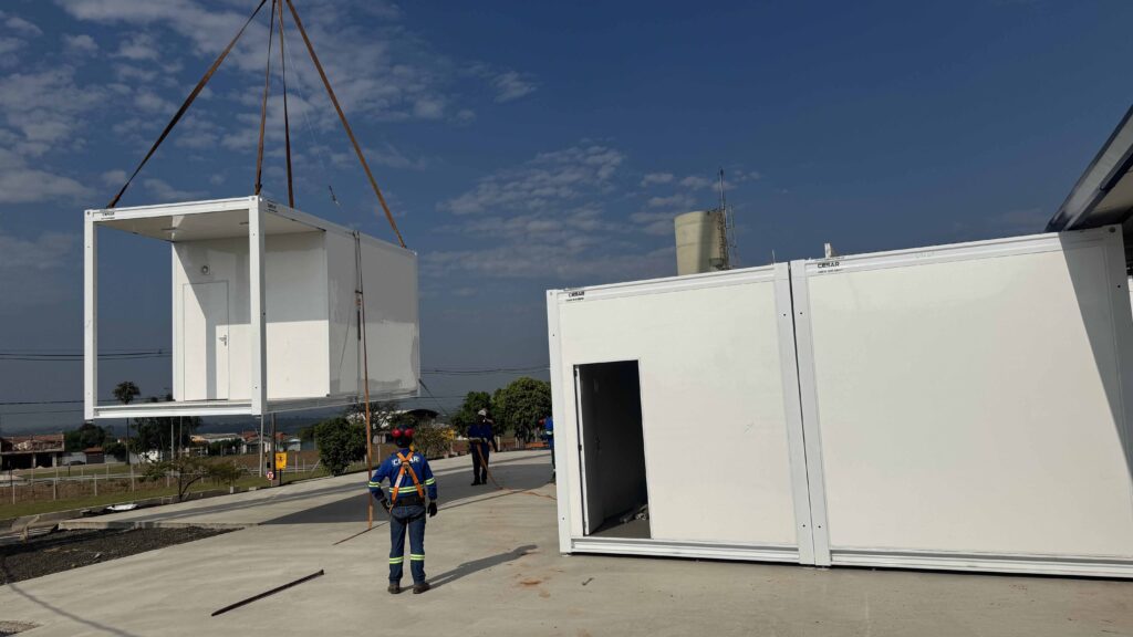 Trabalhadores acompanham a montagem de módulos pré-fabricados em unidade em construção.