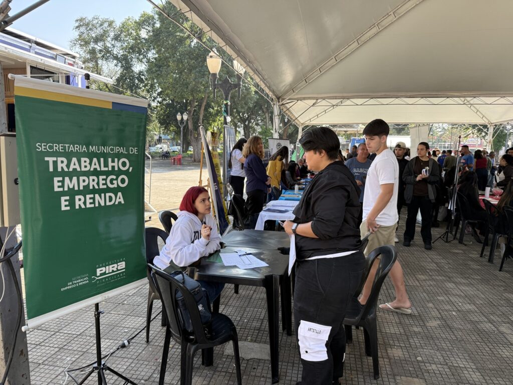 Atendimento da Secretaria Municipal de Trabalho, Emprego e Renda acontece em evento público, com pessoas recebendo orientações e informações sobre oportunidades de emprego em estandes montados sob uma tenda.