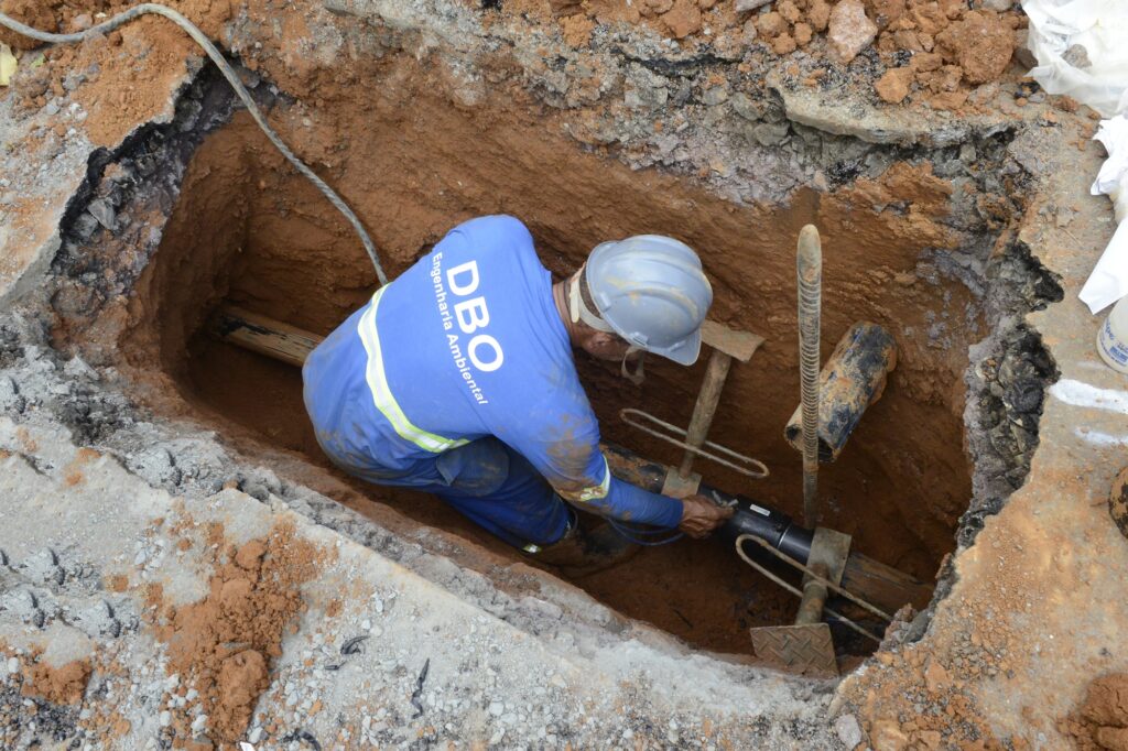 trabalhador realiza serviço em uma vala subterrânea, efetuando a instalação ou conexão de tubulações de abastecimento.