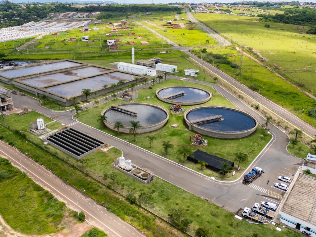 vista aérea de uma estação de tratamento com tanques circulares e retangulares, cercada por áreas verdes e vias urbanas.
