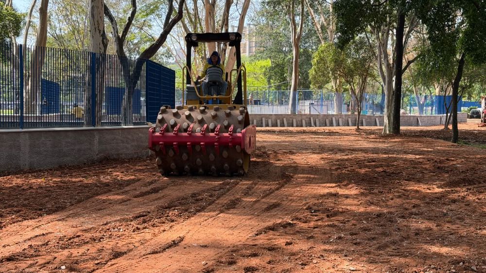 Máquina realiza serviços de compactação e nivelamento do solo para a implantação de um novo estacionamento em área esportiva.