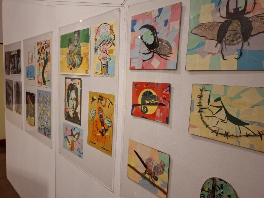 Parede de exposição com obras coloridas de arte contemporânea, caricaturas e representações de insetos em composições criativas.