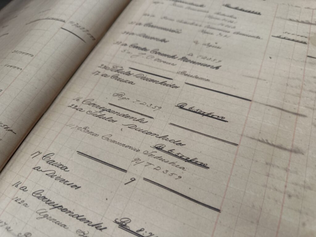 A imagem mostra um livro antigo de contabilidade ou registro administrativo, escrito à mão com tinta sobre papel quadriculado.
