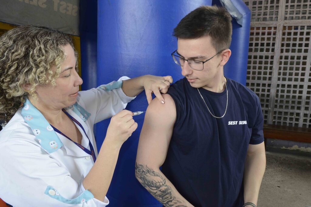 Profissional de saúde aplicando uma vacina no braço de uma pessoa em um ambiente de atendimento, relacionado a uma ação de imunização.