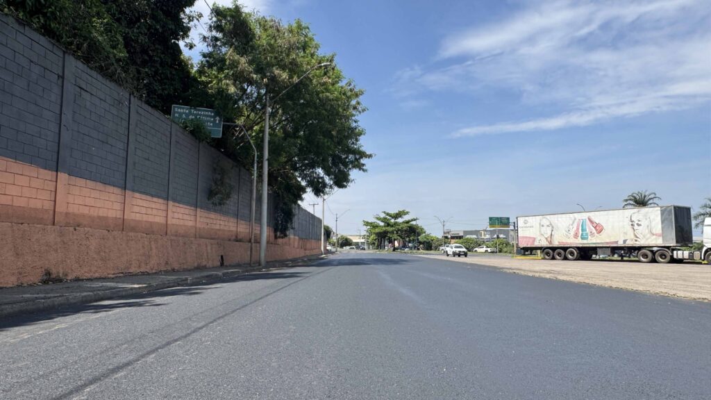 Trecho de recapeamento em execução, mostrando a aplicação da nova camada asfáltica, com cones de sinalização e equipamento de compactação ao fundo.