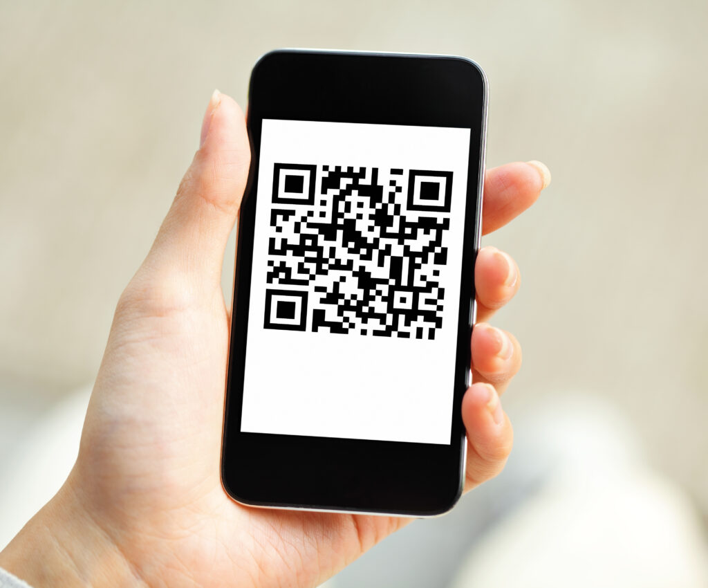 A imagem mostra uma mão segurando um smartphone cuja tela exibe um código QR preto e branco centralizado sobre fundo branco