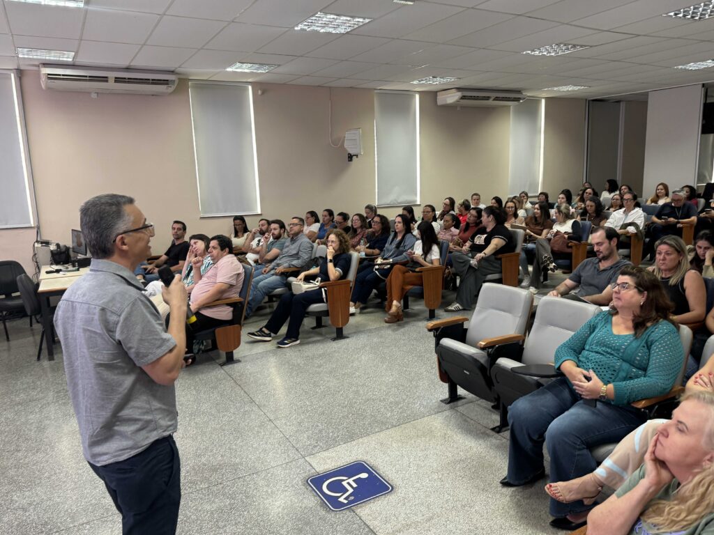 uma pessoa apresenta informações para um público reunido em um auditório, durante um evento ou lançamento de programa, com os participantes acompanhando a exposição.