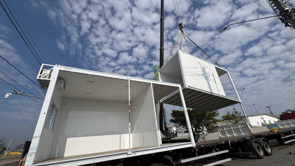 Módulo pré-fabricado é içado por guindaste durante instalação de estrutura modular em área urbana.