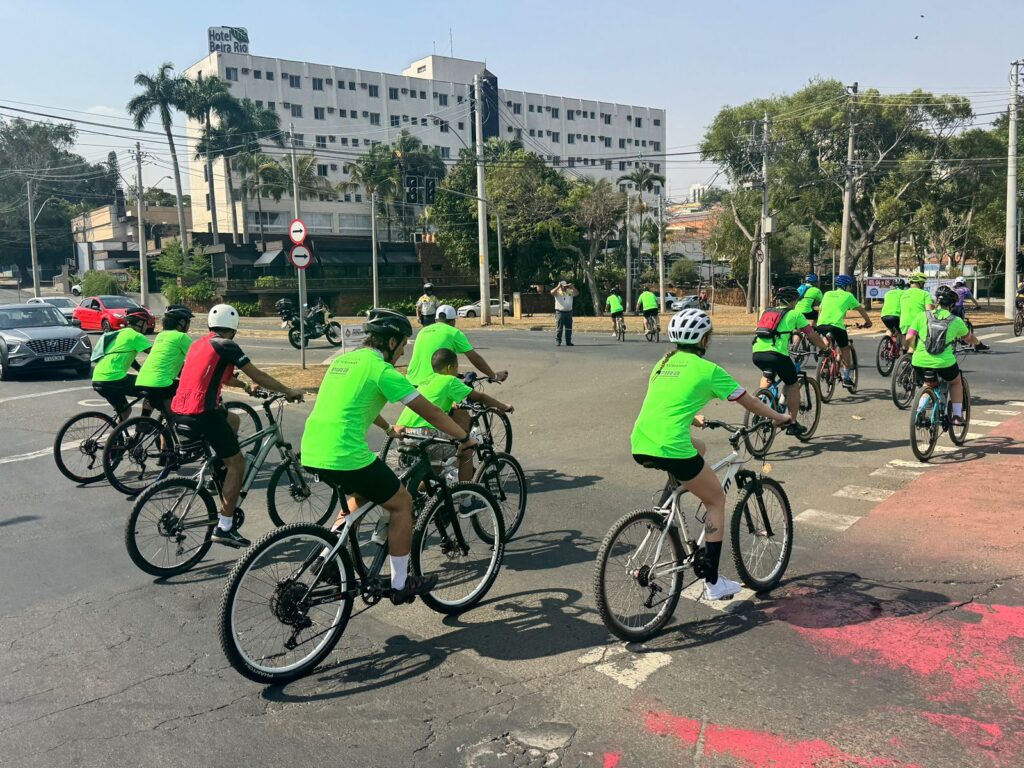 Grupo de ciclistas atravessa cruzamento da cidade em percurso organizado, acompanhado por agentes de trânsito.