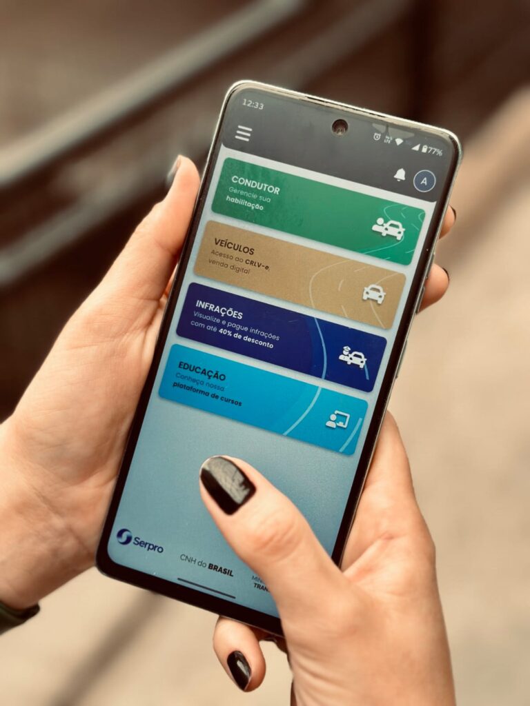 Pessoa segurando um smartphone com o aplicativo CNH Digital/CNH do Brasil aberto, exibindo opções relacionadas a habilitação, veículos, infrações de trânsito e educação para o trânsito.