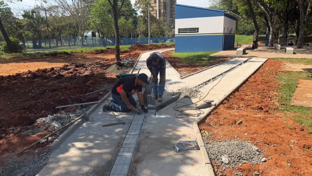 Operários executam a construção de uma pista de caminhada, instalando pisos e acabamentos em um espaço de lazer ao ar livre.