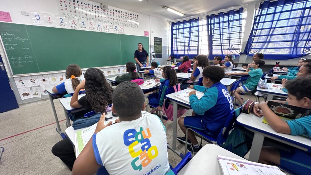 Profissional da área da saúde aplicando ou preparando uma bandagem na mão ou no punho de uma pessoa em um ambiente clínico. A cena mostra um jaleco, um estetoscópio e materiais médicos ao fundo.