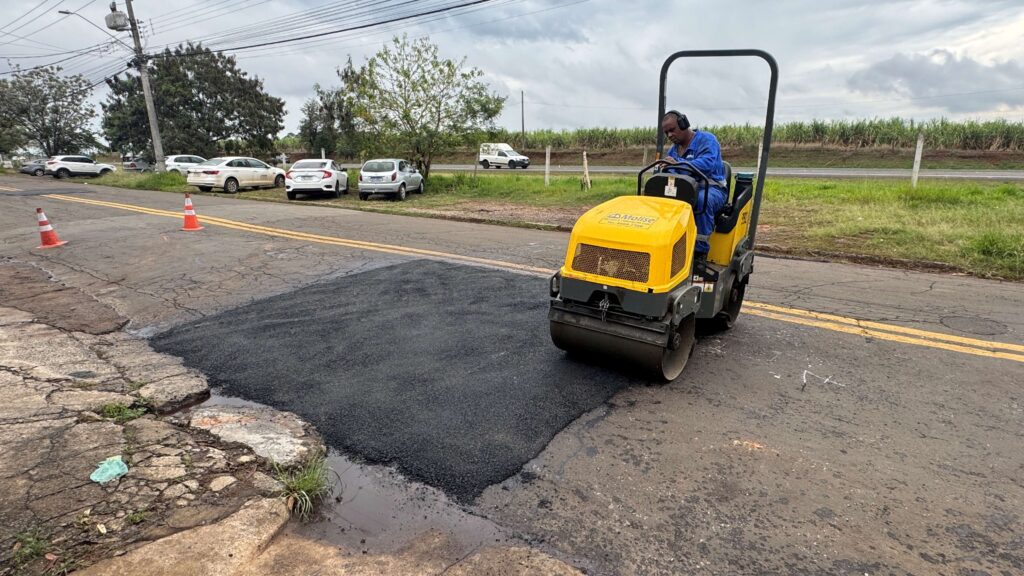 A imagem mostra um trabalho de manutenção de estrada, onde um operário está utilizando um rolo compactador para nivelar uma área asfaltada.