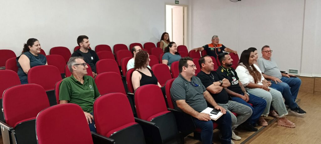 Diversos servidores e gestores da Prefeitura estão assentados em cadeiras vermelhas num auditório, a acompanhar uma reunião de trabalho.