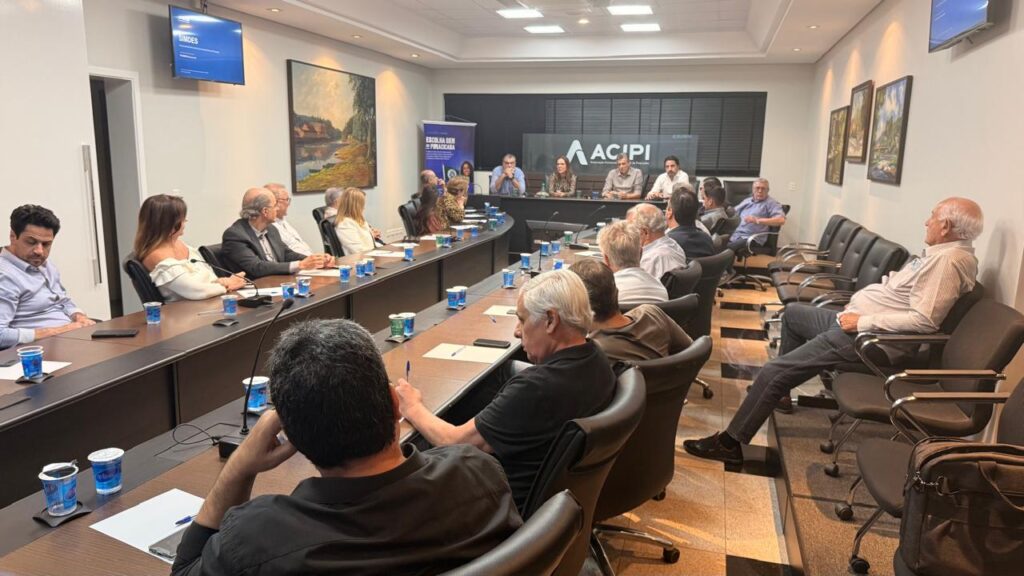 Diversas pessoas e autoridades estão reunidas em redor de uma grande mesa numa sala de conferências da ACIPI para a apresentação das regras do programa Simdes.
