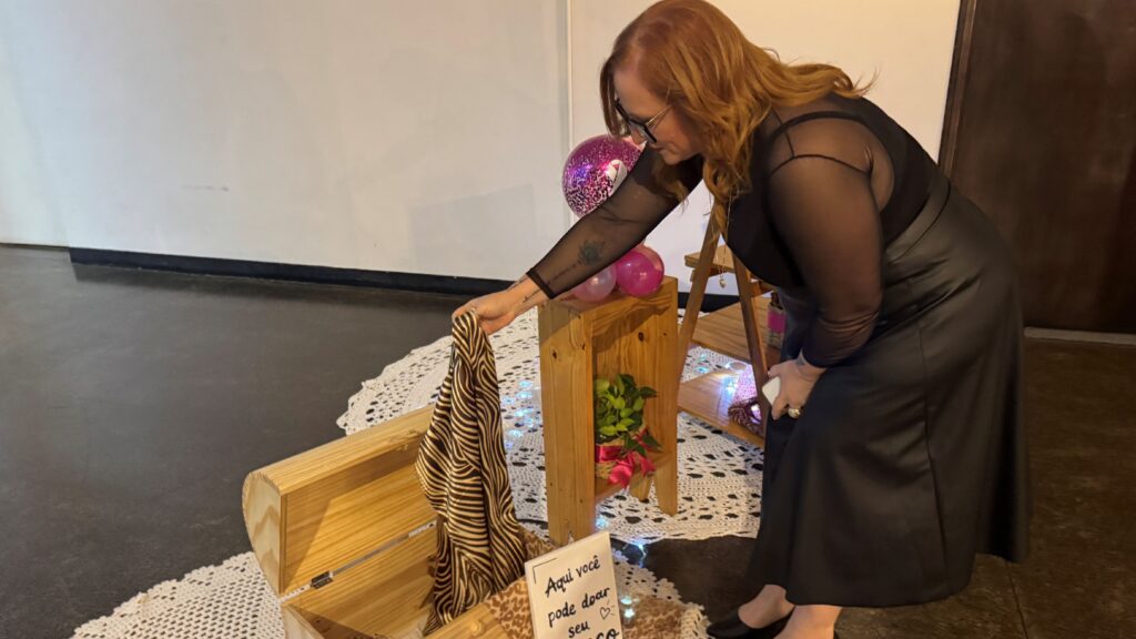Uma mulher deposita um lenço estampado num baú de madeira destinado à arrecadação de doações para o Centro de Oncologia do HFC Saúde.