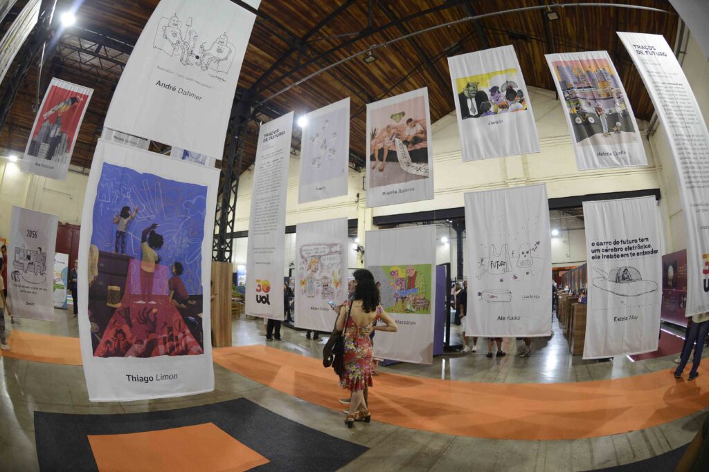 Espaço expositivo do Salão Internacional de Humor de Piracicaba, exibindo painéis e flâmulas com ilustrações e cartuns suspensos ao longo de uma passadeira no galpão do Engenho Central.