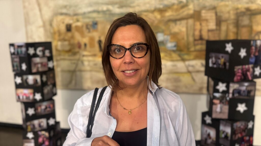 A diretora Daniele Moraes sorri para a câmara no hall do evento, posicionada entre painéis decorativos da Jornada Pedagógica.