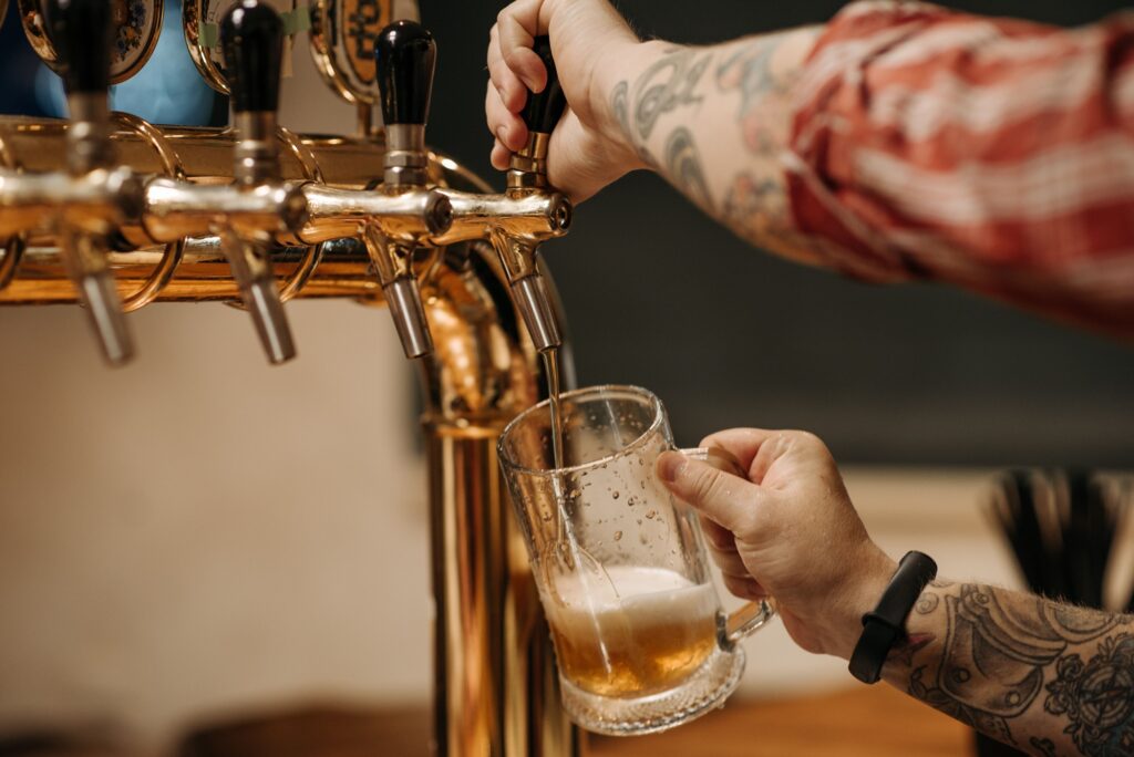 Um plano aproximado de uma pessoa a tirar cerveja à pressão a partir de uma torneira de metal dourada para encher uma caneca de vidro.