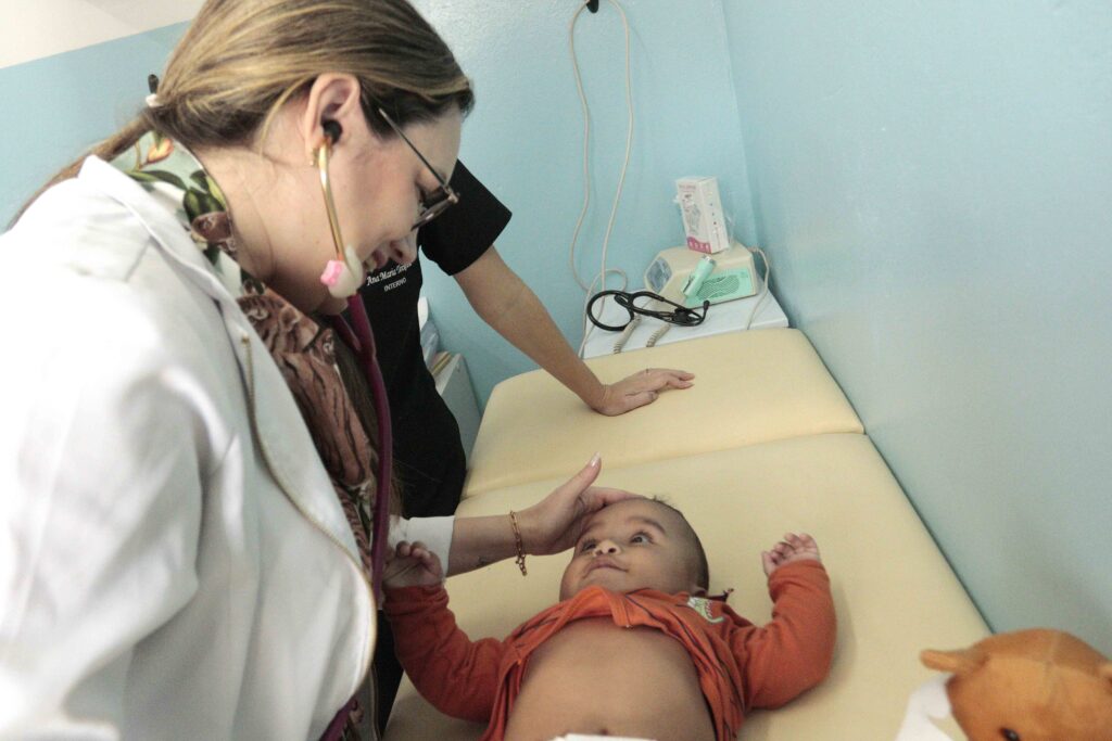 A médica Aimara Fuentes examina carinhosamente o bebé Isaac deitado na maca durante a sua consulta de rotina.