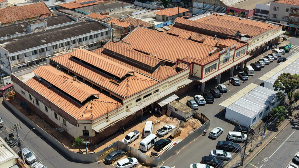 Vista aérea do complexo do Mercado Municipal com a nova cobertura de telhas alaranjadas praticamente concluída, rodeado por ruas e veículos estacionados.