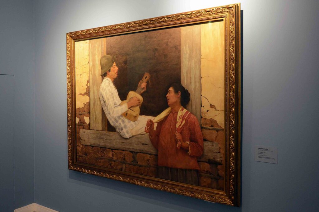 A obra O Violeiro (1899) em destaque numa moldura dourada ornamentada sobre uma parede azul clara.