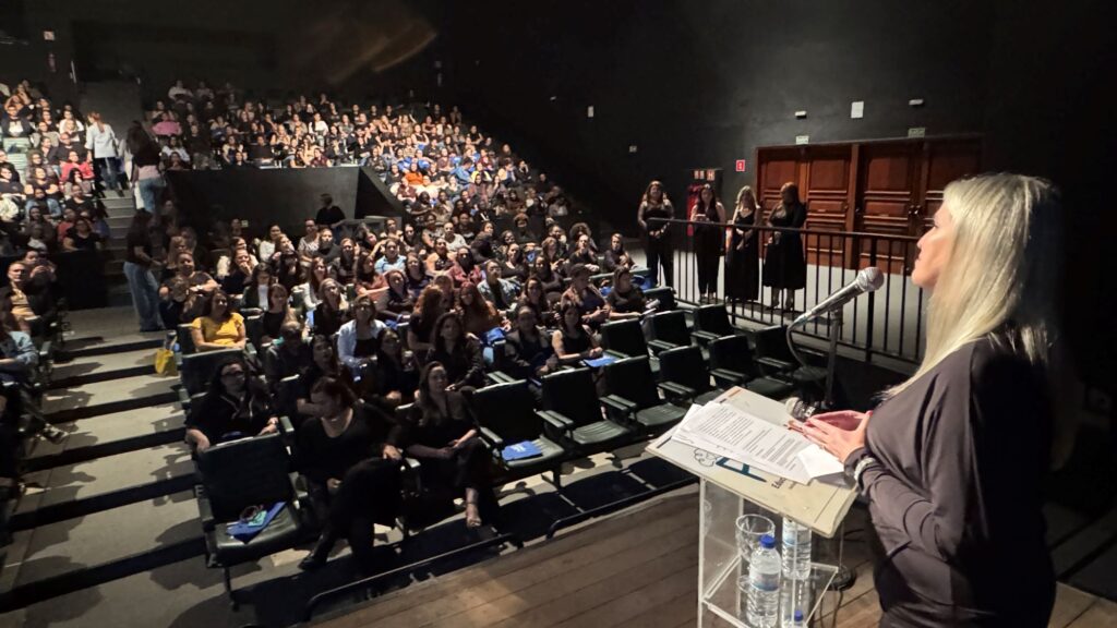 A Secretária de Educação, Juliana Vicentin, discursa num púlpito no palco durante a abertura da Jornada Pedagógica, em frente a um auditório repleto de educadores.
