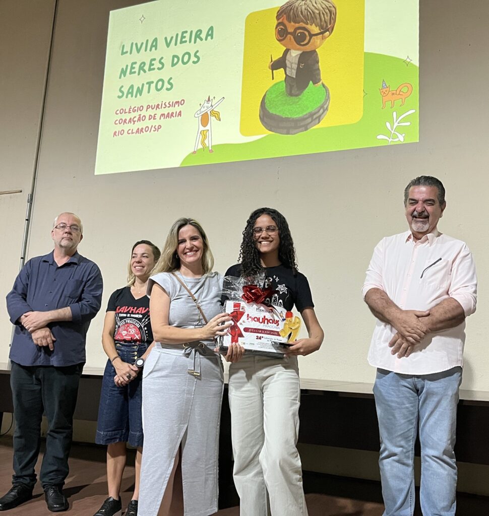 Aline Rossini, da Secretaria Municipal de Educação, faz a entrega do prémio de 3.º lugar a Lívia Vieira Neres dos Santos.