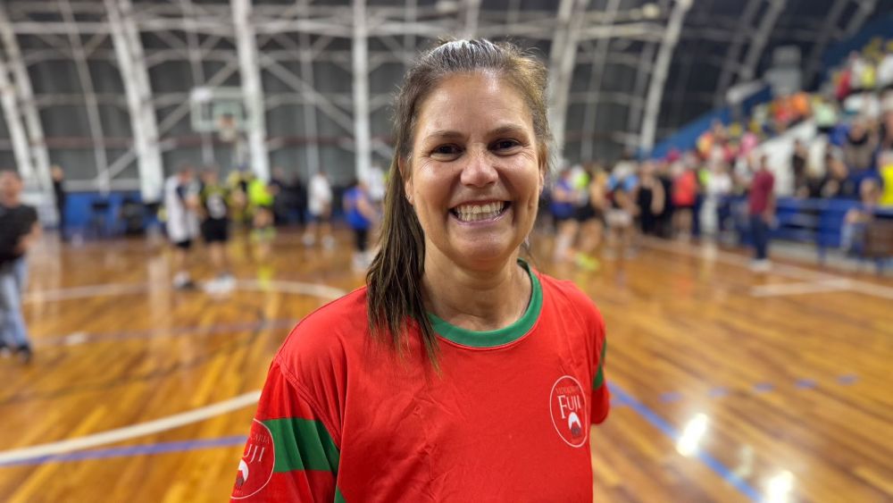 A atleta Ana Vieira de Aguiar sorri para a câmara vestindo a camiseta vermelha e verde do clube Luzitano, no meio da quadra do ginásio polidesportivo.