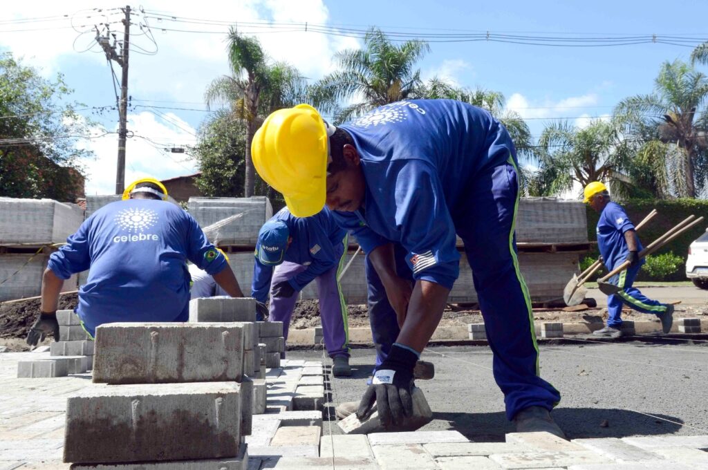 Operário em primeiro plano a encaixar blocos de betão no pavimento com precisão, ladeado por outros membros da equipa de obra.