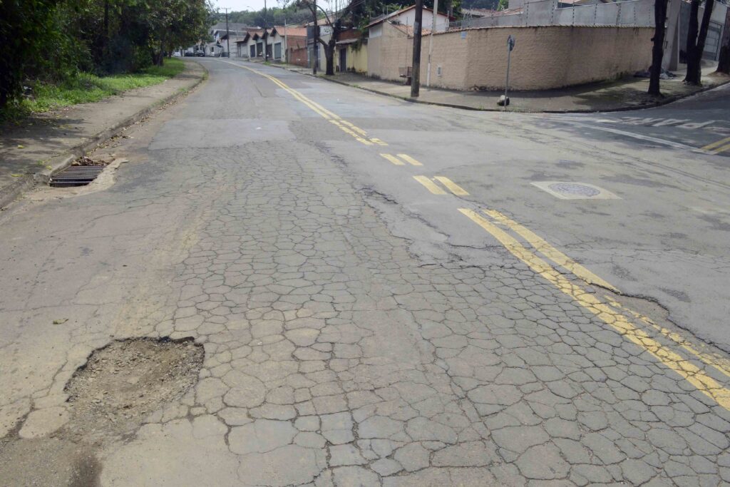 Pavimento asfaltico bastante trincado e desgastado, apresentando falhas e falhas de sinalização de trânsito.