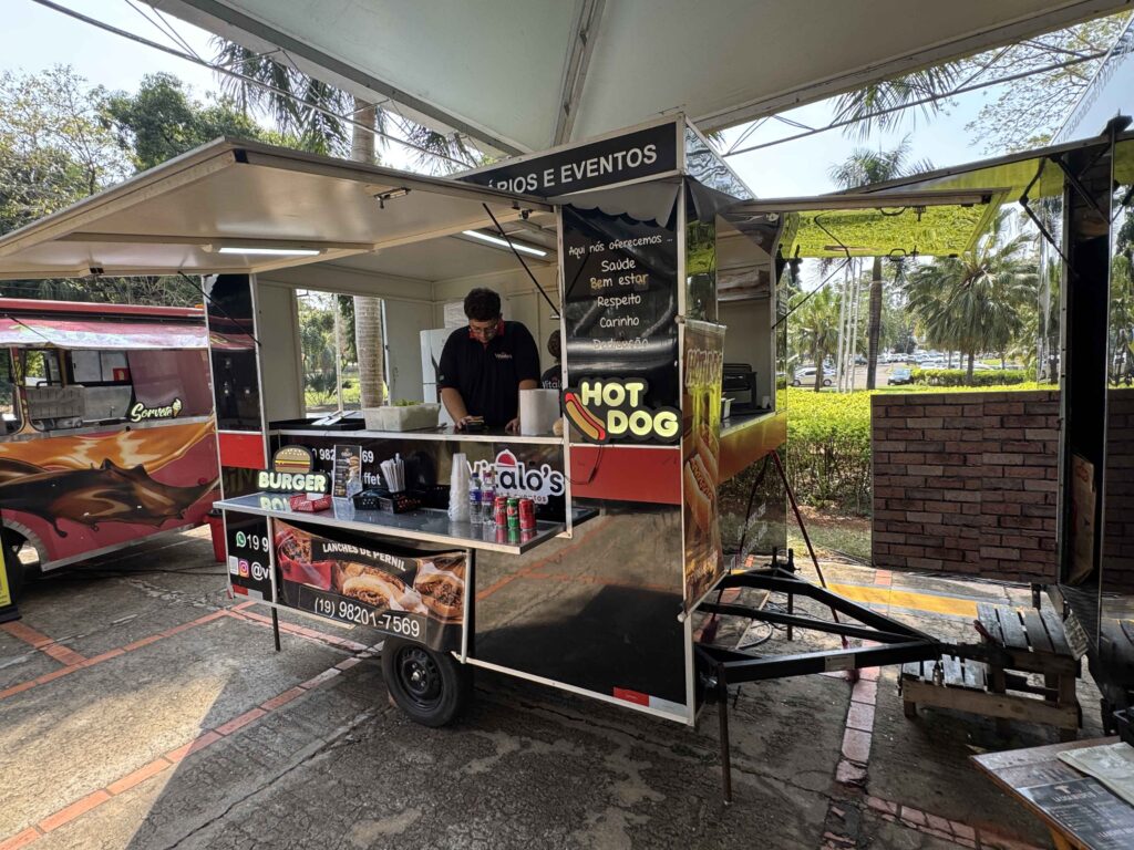 Atendente no interior de um food truck de cachorros-quentes e lanches de pernil estacionado numa área coberta, durante o evento gastronómico "Sabores na Rua".