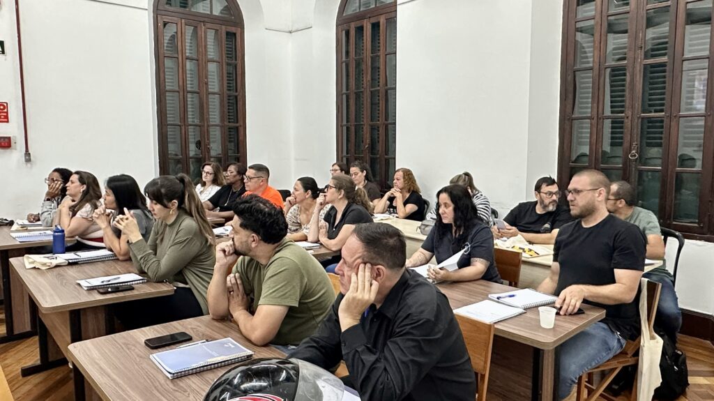 Mostra um plano mais aproximado dos alunos sentados nas carteiras em estilo auditório, concentrados e a acompanhar a explicação durante a aula do curso.