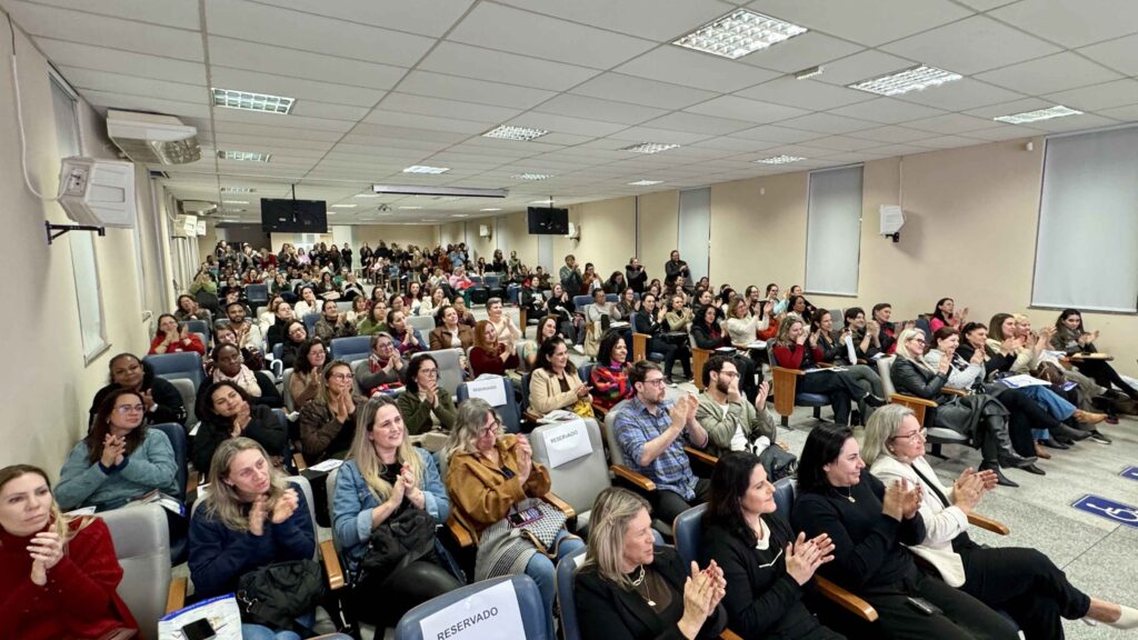 Plateia lotada num auditório assistindo e aplaudindo uma apresentação durante a Jornada Pedagógica Inclusiva.