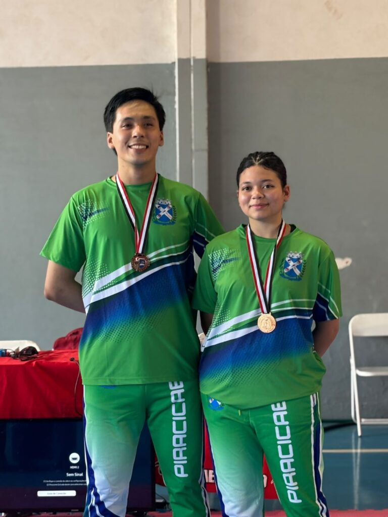 Dupla de atletas de taekwondo vestindo o equipamento oficial da cidade e exibindo as medalhas de bronze obtidas na modalidade poomsae.