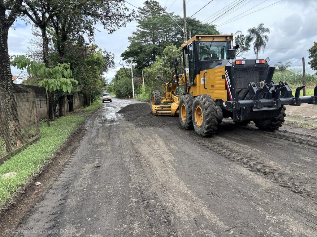 A motoniveladora amarela trabalha no espalhamento de material fresado (asfalto triturado) sobre uma estrada de terra batida para melhorar a sua pavimentação