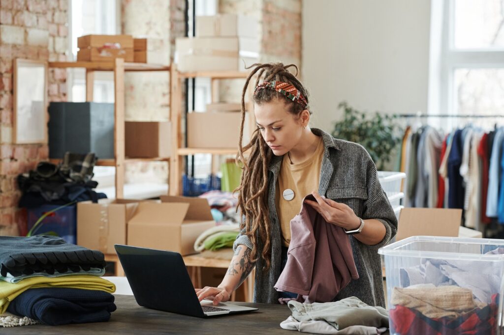 Uma jovem empreendedora com dreadlocks trabalha num ambiente que parece ser um armazém de roupas ou escritório de e-commerce
