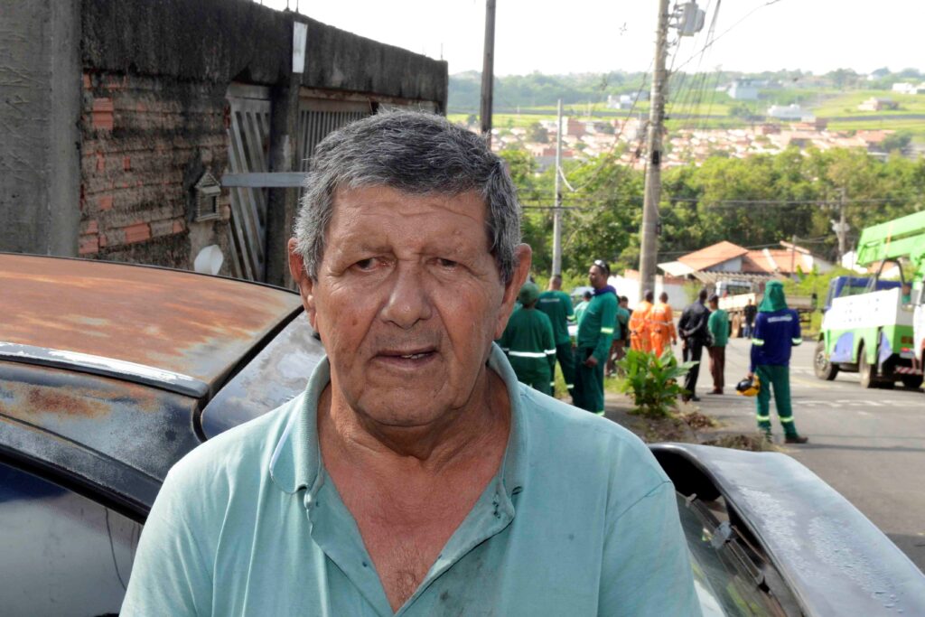 Retrato em plano aproximado do morador José Eduardo de Almeida. Ao fundo, é possível ver trabalhadores de limpeza/zeladoria e veículos de apoio na rua