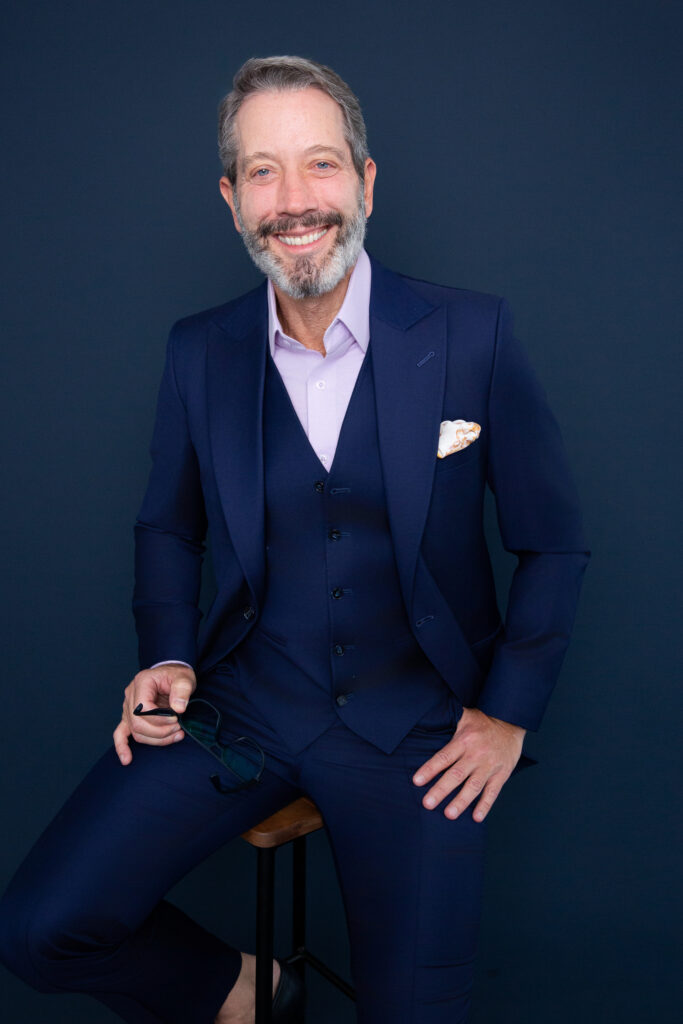 Foto de estúdio do palestrante e psicoterapeuta Leo Fraiman, sorridente e vestindo um fato azul-marinho de três peças.