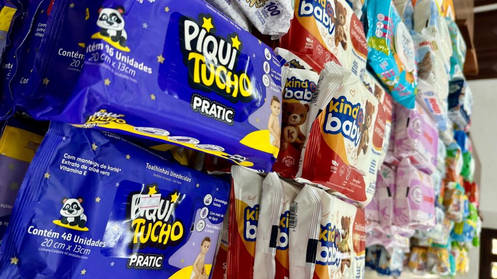 Várias embalagens de toalhinhas umedecidas infantis (como as marcas Piquitucho e Kinda Baby) empilhadas e dispostas em prateleiras.