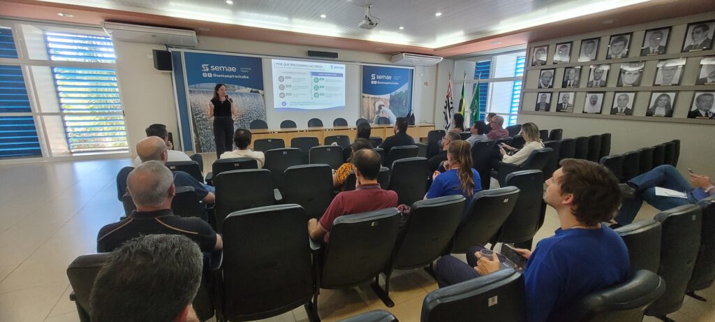 Natássia Bonini, gerente Ambiental do Semae, realiza uma apresentação para as lideranças da autarquia no auditório, explicando as etapas de elaboração do Plano Municipal de Segurança da Água (PMSA) enquanto a plateia acompanha o slide projectado na tela.