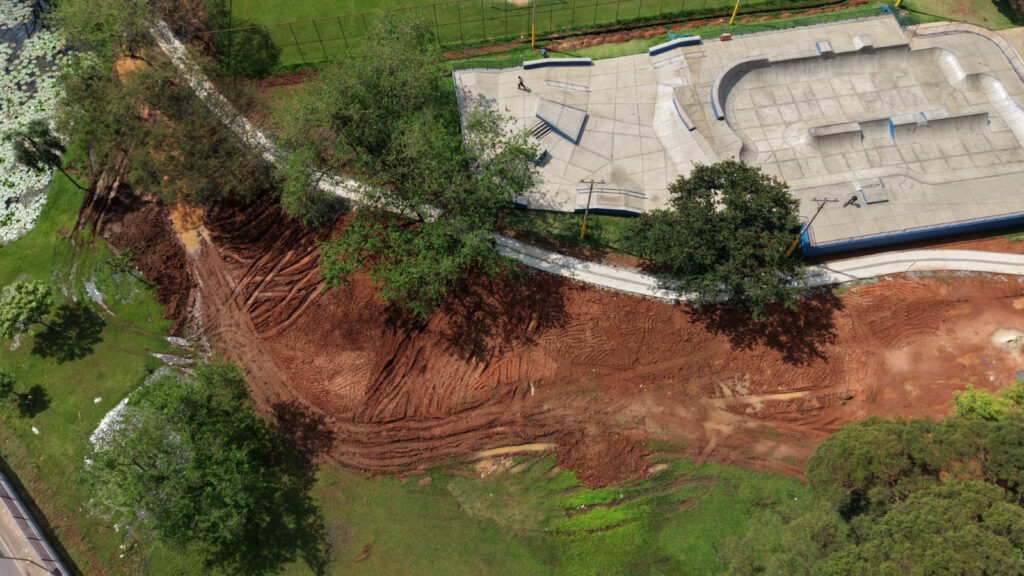 Vista aérea do complexo de lazer destacando a pista de skate de cimento, o traçado da pista de caminhada e a área de terra batida onde decorrem as obras para a construção da nova pista de pump track.