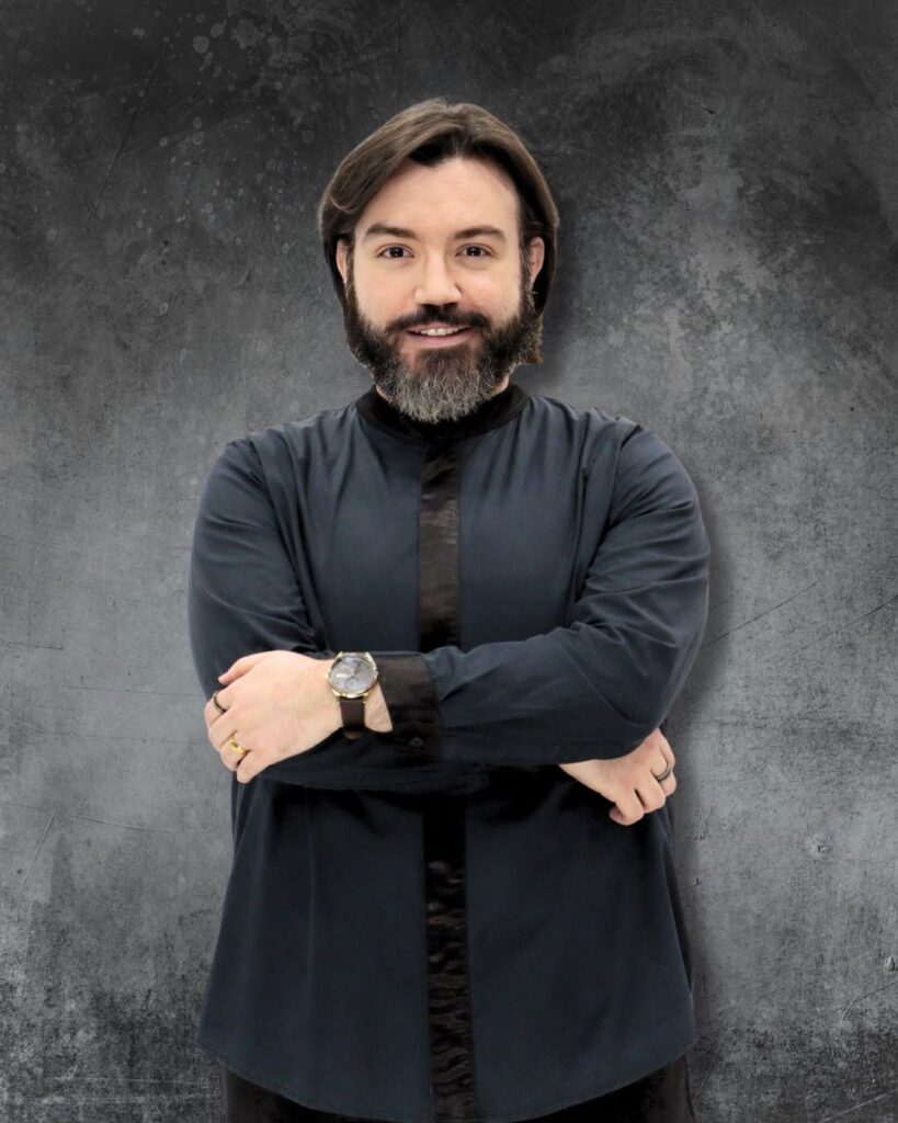 A imagem apresenta um retrato do maestro Lucas Lopes sobre um fundo cinzento com textura de cimento